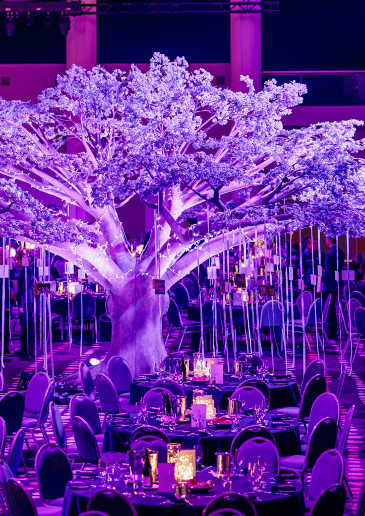 Purple lighting illuminates a tree and perfectly laid tables at a Lo Key Agency planned brand activation event